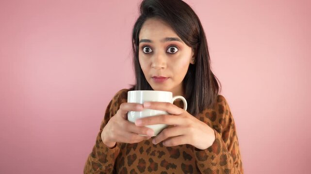 Close up of happy shocked amazed pretty young Asian woman girl hold cup drinking enjoy coffee feels happiness look at camera, isolated over light pink studio background.