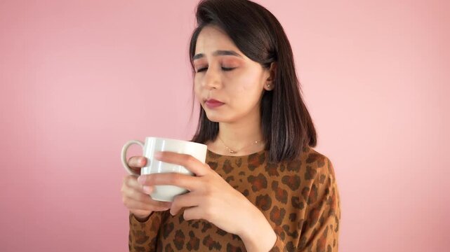 Close up of upset unhappy young Asian woman girl hold cup in hands drinking coffee thinking reflection feels worried nervousness, isolated over light pink studio background.