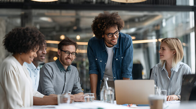 Diverse team collaborates around a modern conference table. One member leans forward, actively engaging with colleagues. Laptops, glasses, and documents sit on the table