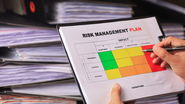 Attentive professional filling out detailed workplace safety risk assessment matrix document on clipboard with pen near stacked folder