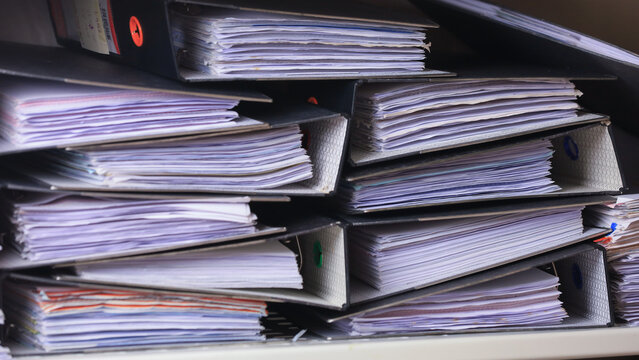 Heavy stack of paperwork binder document showing stressful workplace safety risk assessment requirement needing urgent careful organization