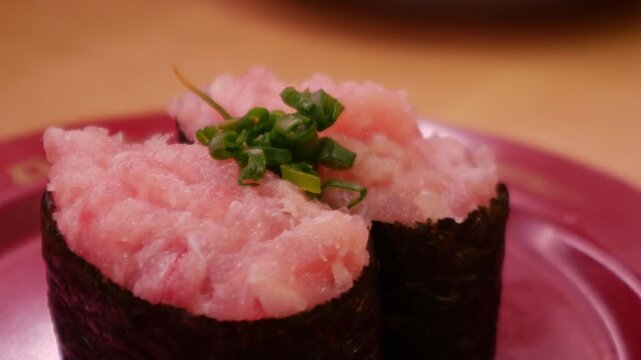 Negitoro minced fatty tuna gunkan maki sushi topped with green onion on red plate, Japanese restaurant