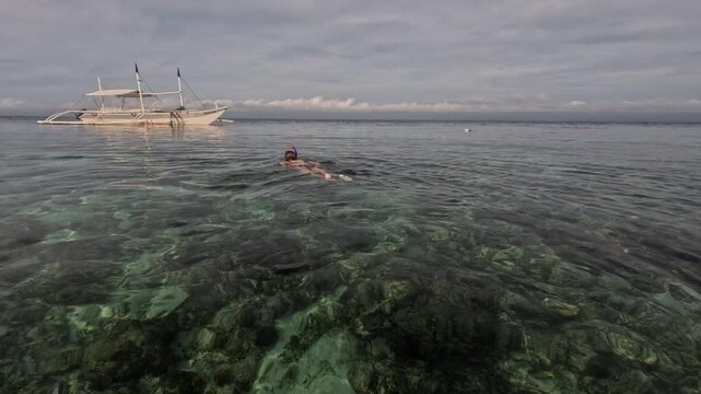 Woman snorkeling in clear tropical water with traditional Filipino boat at Tubod Beach Siquijor Philippines