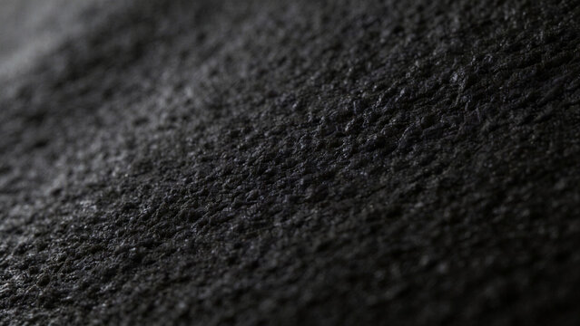 Abstract macro photography of dark textured surface with charcoal grey color palette, fine rough grain pattern, matte finish and subtle side lighting creating uniform composition for minimalist...