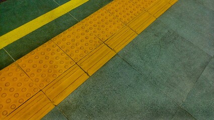 Top view of yellow tactile paving for the visually impaired on a train station platform. Safety floor tiles in a public transportation hub at night © Jassem