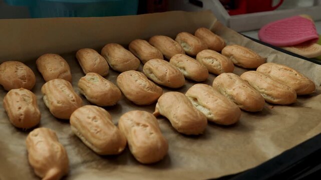 Baked choux pastries arranged on trays in sunny kitchen. Preparation stage for custard cream filling in dessert making process. video footage video footage photography