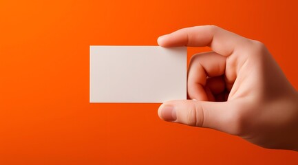 Fototapeta premium A hand holding a blank business card against a vibrant orange background, perfect for customized branding or marketing designs.