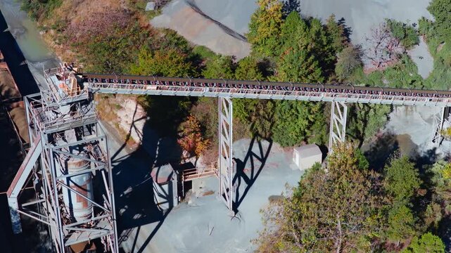 Long conveyor belt transporting aggregate across quarry processing facility, aerial tracking right from freight train to hopper with dump truck