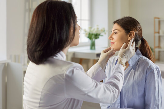 Dermatologist with broad expertise examines patient. Doctor in gloves looking at woman's face during dermatology consultation visit at clinic, performing skin examination with gentle touch