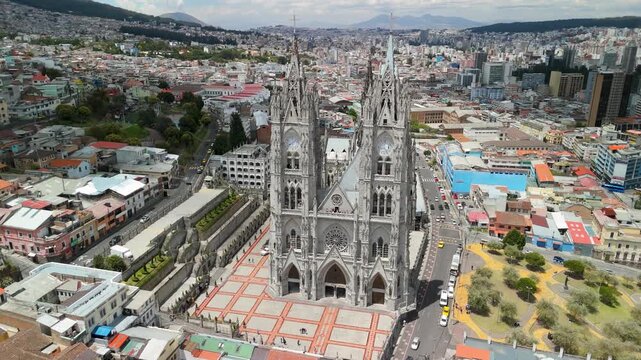 Aerial parallax orbits full Bas&iacute;lica del Voto Nacional neo-gothic twin spires flying buttresses forecourt plaza against Quito cityscape