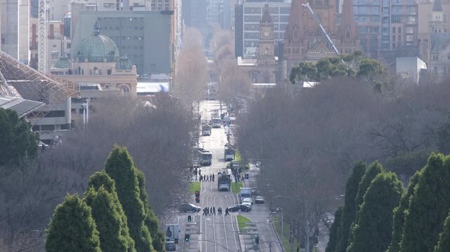 St Kilda road traffic in central Melbourne, Australia, with trams and cars moving along the major city avenue. Urban street framed by winter trees with historic and modern architecture in CBD skyline.
