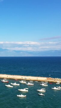 Small boats float in a tranquil harbor with deep blue sea and distant mountains under a clear sky in Koroni, Greece.