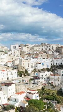 Scenic view of traditional whitewashed buildings clustered on a hillside under a dramatic cloudy sky in Peschici, Italy. Mediterranean architecture and charming village atmosphere are highlighted.