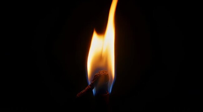 Close up image of a burning matchstick in a dark environment showing fire