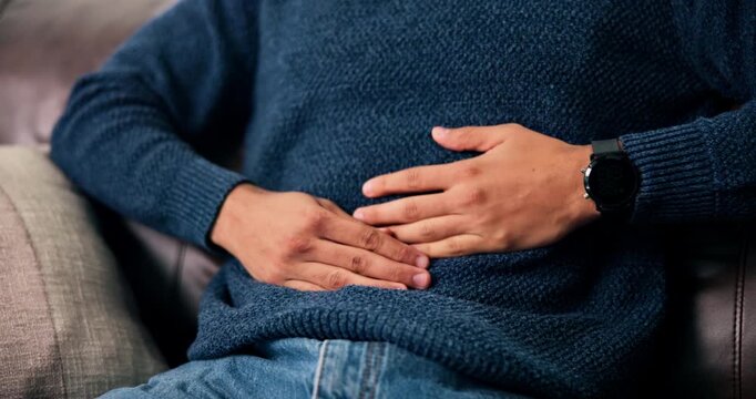 Hands, stomach pain and man on sofa in home with indigestion, diarrhea or constipation in living room. Abdomen, sick and male person with belly ache for food poisoning or illness in apartment.