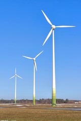 Fototapeta premium Wind turbines turning beneath a bright blue sky on a sunny day. Renewable energy technology producing clean electricity in a calm open landscape.