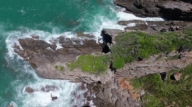 Turquoise ocean waves breaking on rugged rock formations at Po&ccedil;a da Tartaruga coastline in Arma&ccedil;&atilde;o dos B&uacute;zios, Rio de Janeiro State, Brazil, aerial shot