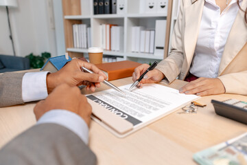 A real estate agent and client discussing property sale details at the office table, reviewing and signing home purchase contracts with miniature house models and money on the desk.