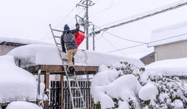 雪国の生活：吹雪の中、車庫がつぶれないように雪下ろしをする