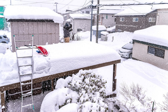 雪国の生活：吹雪の中、車庫がつぶれないように雪下ろしをする
