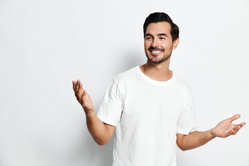 Fototapeta premium Smiling young man wear white t-shirt look cheerful while standing against plain light background with open hands expressing joy and friendliness.