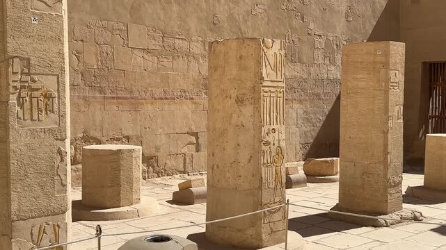 A detailed medium shot of ancient limestone pillars with hieroglyphic inscriptions and wall reliefs inside the Temple of Hatshepsut in Luxor Egypt