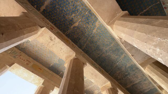Low angle view of the vibrant blue painted ceiling with golden stars and massive columns inside the Temple of Hatshepsut at Deir el-Bahari in Egypt