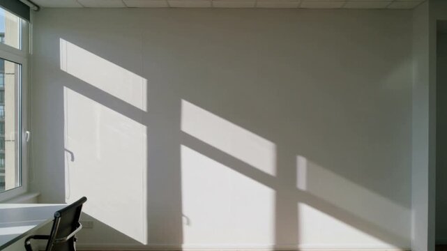 Sunlight creating shadows on a white wall in an empty room.