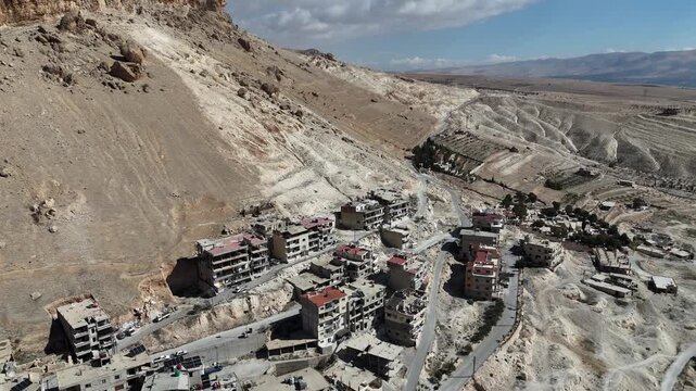 Aerial drone view of Ma'loula, Syria, an ancient village nestled at the foot of steep mountain cliffs, featuring unique architecture and winding roads