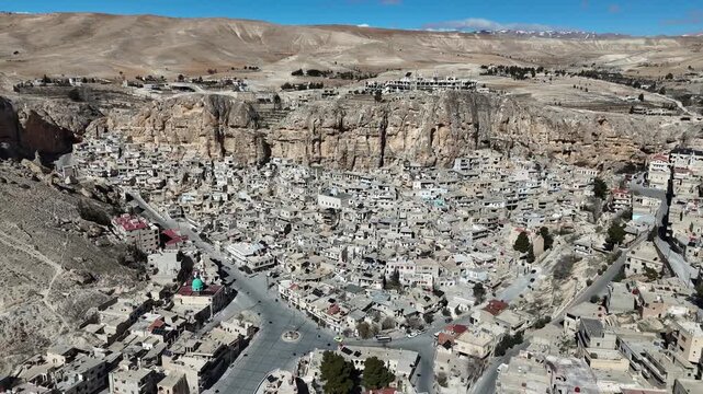 A wide aerial drone shot of the ancient village of Ma'loula, Syria, showcasing its unique architecture built into the rocky mountain cliffs