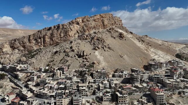 Panoramic drone vista of the historic town of Ma'loula, Syria, highlighting its dramatic geographical setting within the rocky peaks of the Qalamoun range