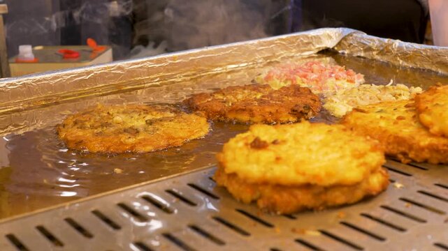 Slow motion close-up of crispy Bindaetteok seafood pancake street food cooking on hot grill stove top with oil at Gwangjang night markets in Seoul city South Korea traditional cuisine culinary snack