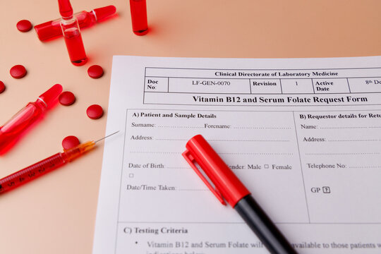 Close up of B12 vials, red tablets and blood test request on a cream gradient background for professional healthcare and diagnostics.