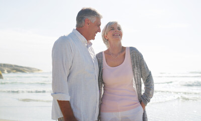 Fototapeta premium Vacation, couple and relax with laugh at beach for romantic getaway, funny chat and bonding. Holiday, mature people and talking at seaside with weekend break, healthy relationship and humor on space