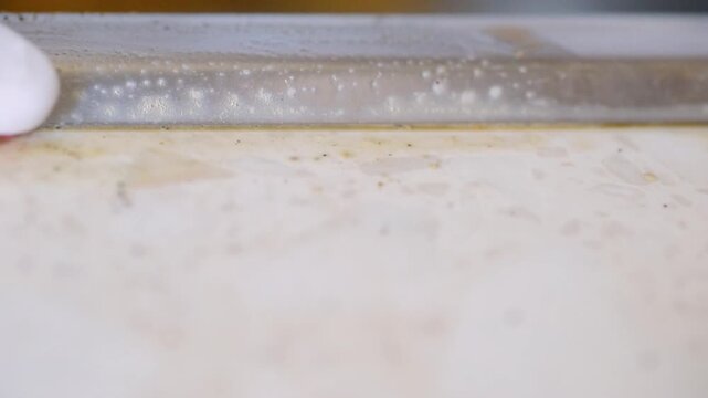 Closeup sink caulk scrubbed with toothbrush, professionalstyle degreasing and scum removal along stainless trim methodical strokes with foaming soap, bristles working at seam