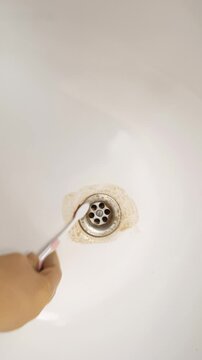 Closeup sink drain being scrubbed around rim with small brush brown rust ring loosens as gentle circular strokes target crevice buildup hand works precisely, alternates scrubbing