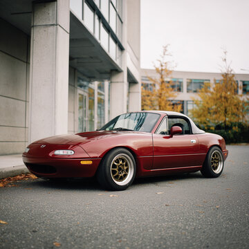 Roter Mazda MX-5 Miata (Eunos Roadster) als Cabrio vor moderner Architektur. Klassischer japanischer Sportwagen, Editorial-Motiv f&uuml;r Automobil, Design, Fahrspa&szlig; und Roadster-Kultur.
