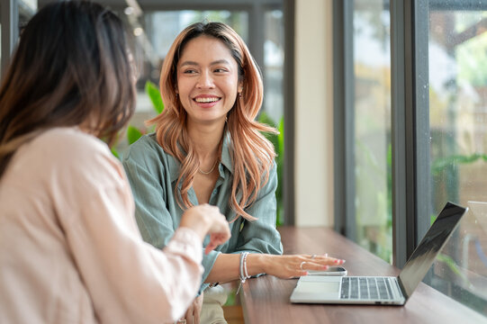 Pretty asian woman talking to friend aside laptop while meetup for work or study at counter in cafe