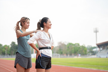 Fototapeta premium Asian woman massaging a friend's shoulder before running exercising on racetrack in sports stadium.