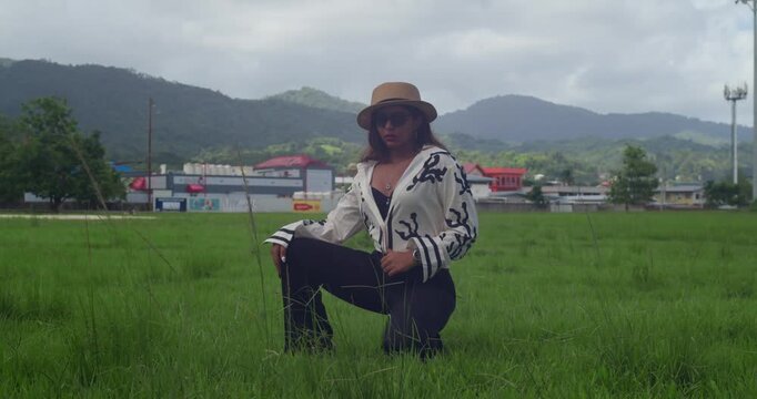 Dressed for work in tan slacks and a white shirt, a girl wears a sun hat and reads in a mountain-side park during her lunch break.