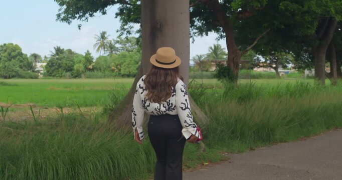A girl in a black vest and matching trousers wears a stylish panama hat while reading in a scenic park with a massive mountain range in view.