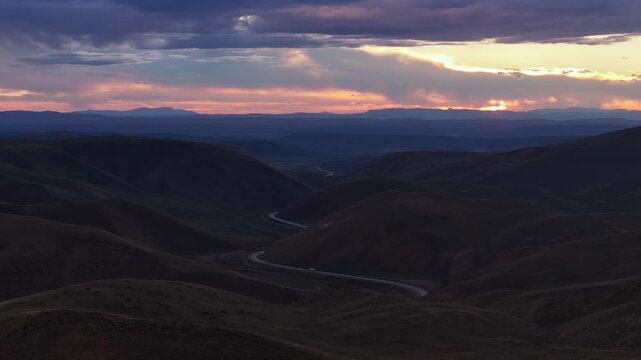 Paved road cutting across rolling desert terrain beneath colorful dusk sky