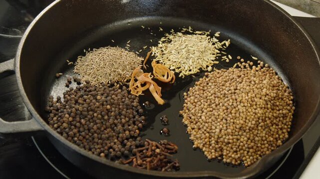 Mace, cardamom, star anise, cinnamon added to spices in cast iron pan