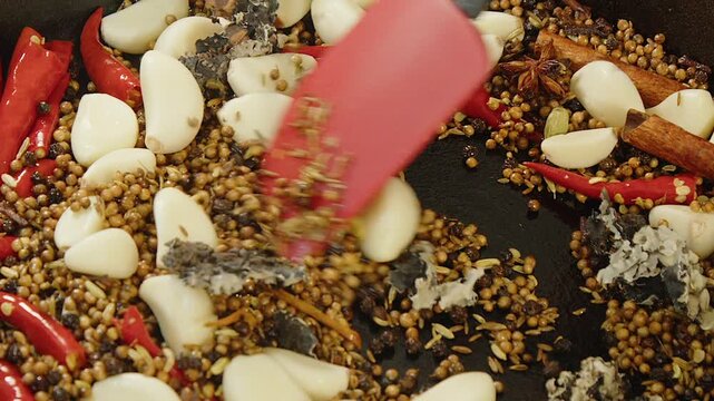 Close up garlic, hot chili are stirred into whole spices in masala pan