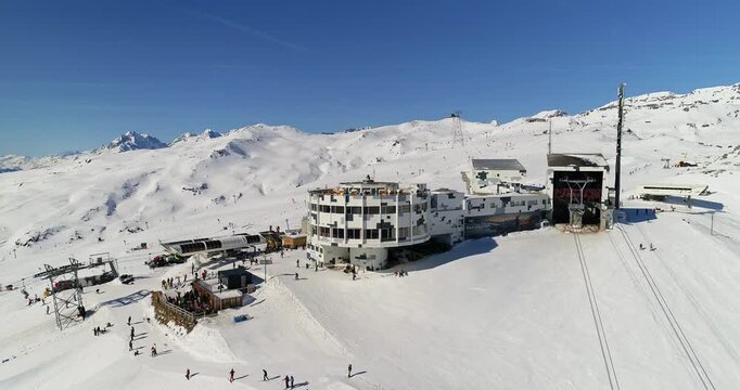 Cinematic drone orbit around a ski lift station in LAAX with alpine terrain and snowpark slopes surrounding the building. Dynamic aerial movement and authentic Swiss winter resort atmosphere.