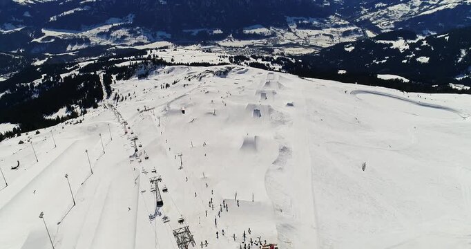 High aerial drone shot overlooking the LAAX snowpark with jumps, rails, and groomed lines visible across the slope. Wide alpine panorama and cinematic winter sports landscape.
