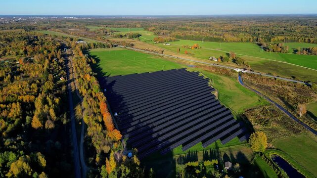 Aerial parallax shot of solar panel farm surrounded by colorful autumn trees and green farmland in rural countryside