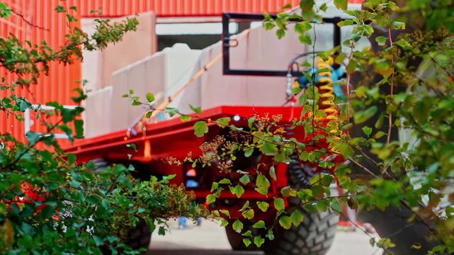 Slow motion static shot of red flatbed trailer loaded with concrete blocks driving past industrial warehouse through foliage