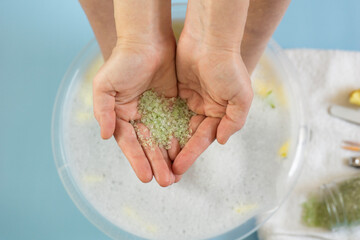 Obraz na płótnie Canvas top view of person holding green sea salt in cupped hands over a bubble bath basin with yellow petals, concept of spa salon, concept of wellness center, concept of beauty treatment