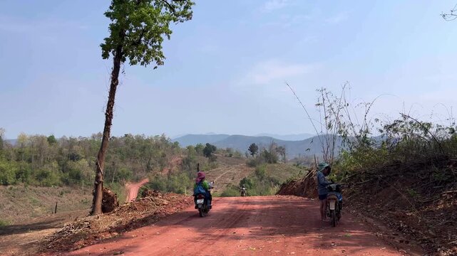 Simple rural life of local villagers traveling on a red dirt road in a remote mountain area